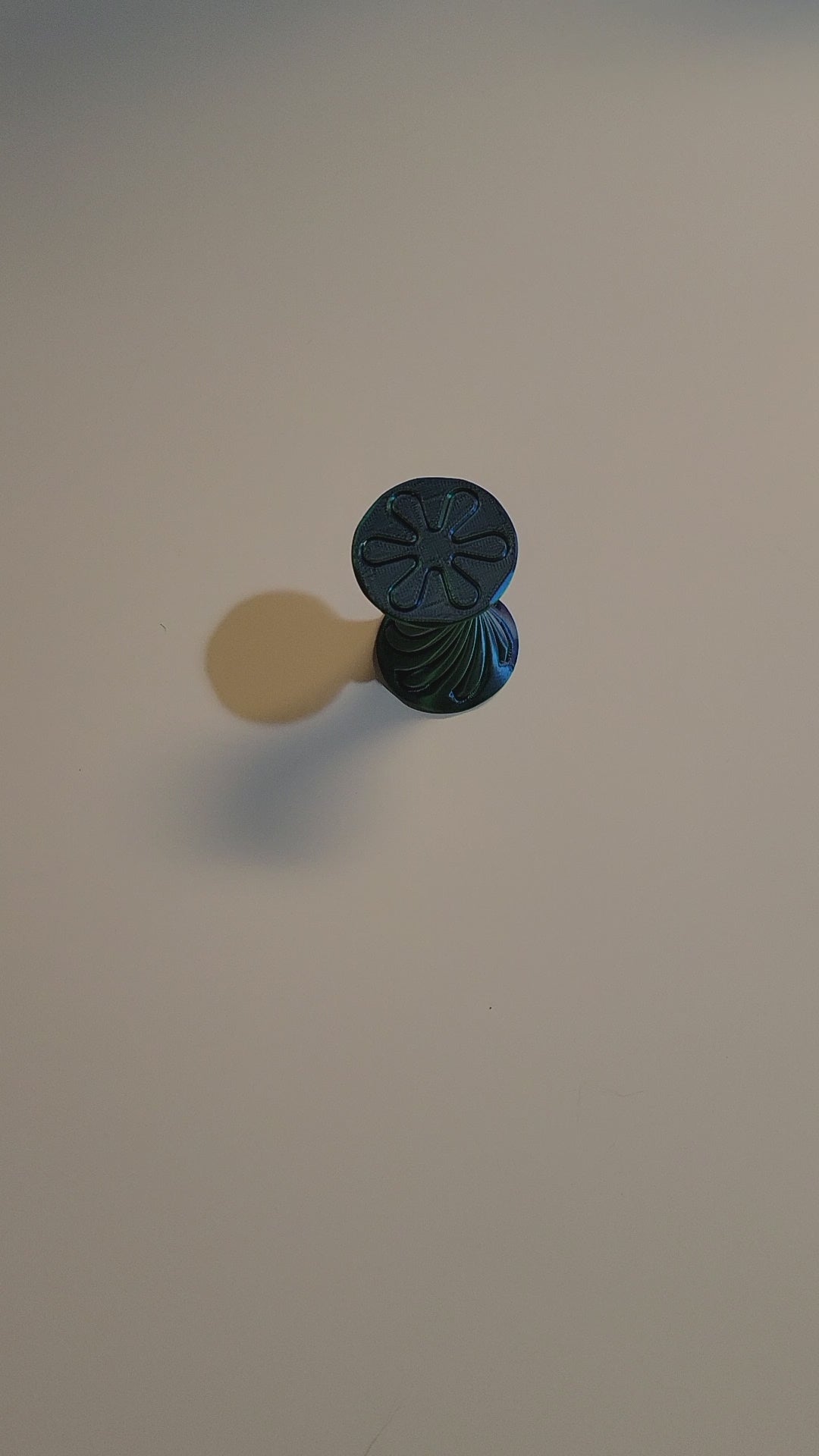 Blue to Green Silk color-shifting 3D-printed hourglass interlock fidget shown twisting outward until locking in at full extension by 2 hands on light grey backdrop.