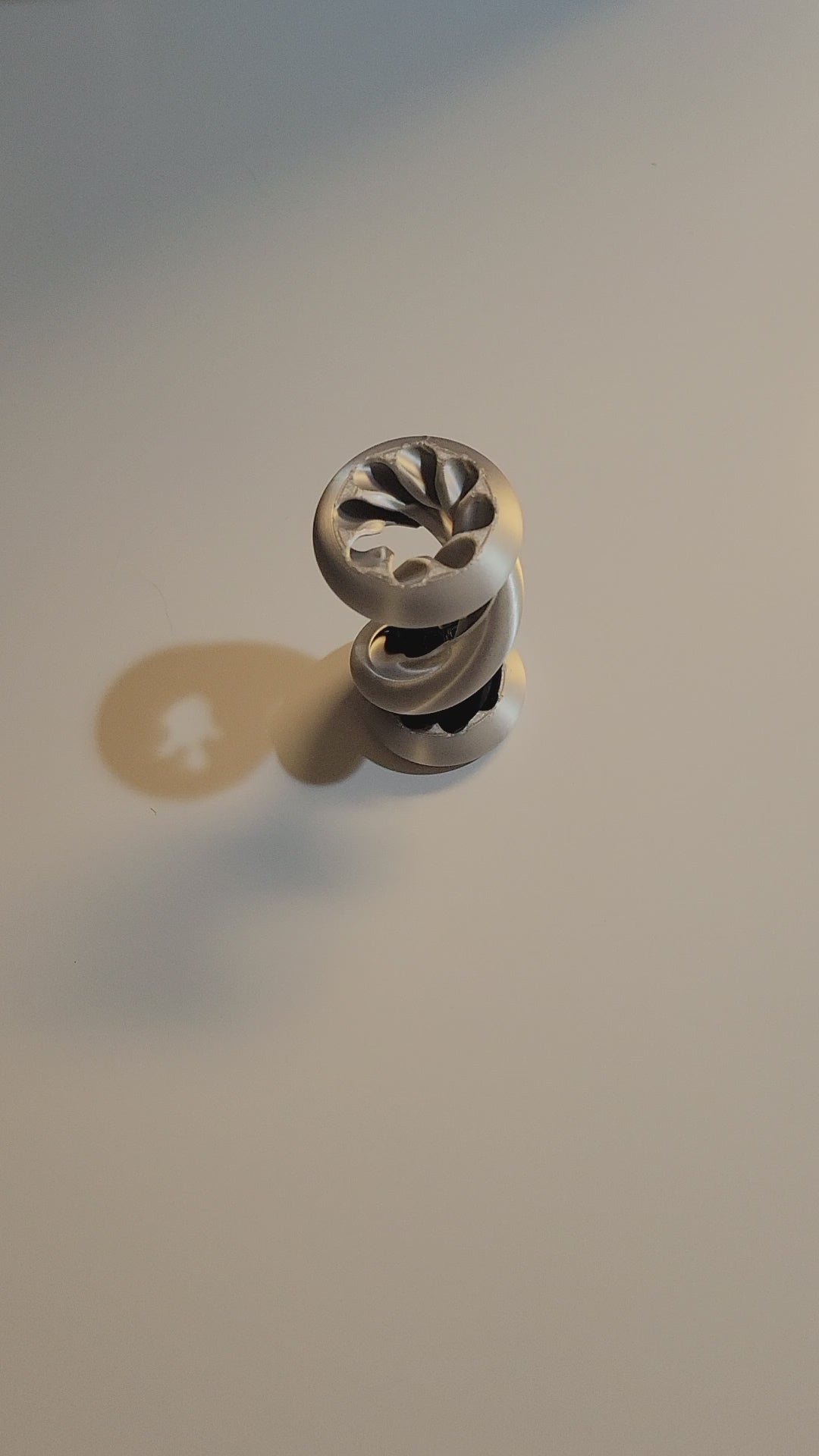 Silver Silk and Onyx Black 3D-printed Gravity track fidget with 2 hands displaying ball dropping twisted track and passthrough function on light grey background. 