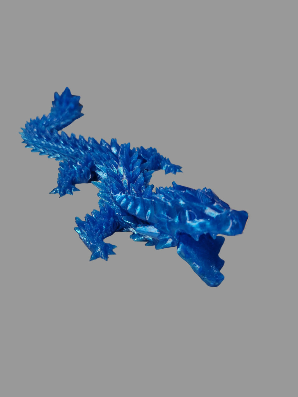 Translucent Blue 3D-printed wingless articulated dragon with crystalized jagged scales and open jaw on gray backdrop.