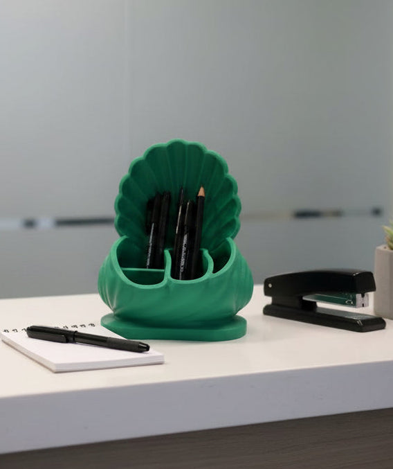 Emerald Green 3D-printed scallop shell inspired desk organizer sitting on a white desktop filled with pens next to a stapler and notebook.