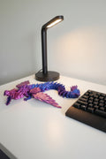 Blue to Purple Silk color-shifting fully articulated 3D-printed dragon on a desk next to a black lamp and keyboard.