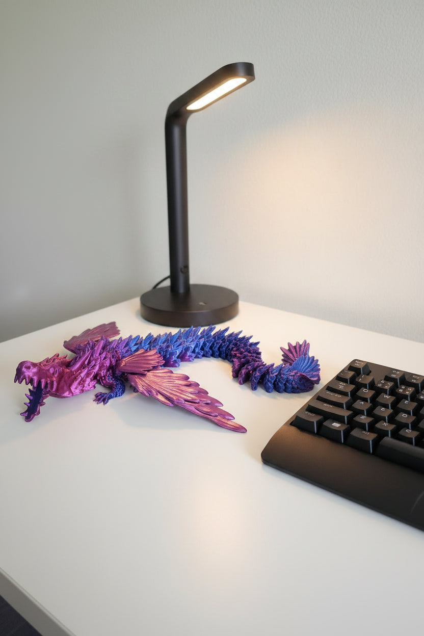 Blue to Purple Silk color-shifting fully articulated 3D-printed dragon on a desk next to a black lamp and keyboard.