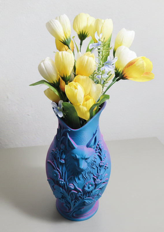 Teal to Pink color-shifting 3D-printed vase with intricate cat and floral design holding yellow flowers on a gray background.
