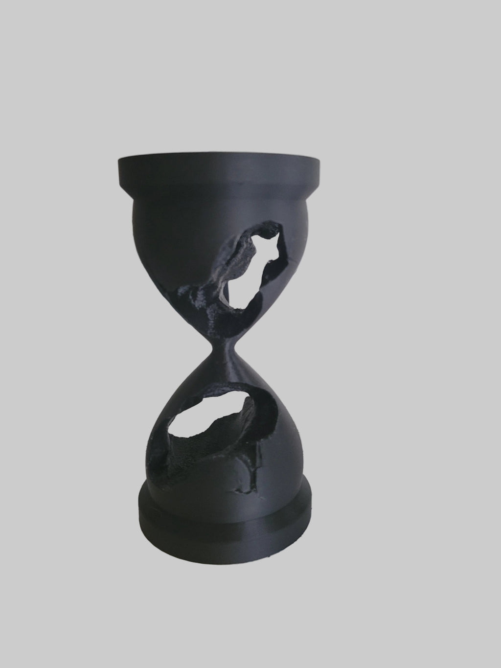 Onyx Black 3D-printed fractured hourglass sculpture with weather-textured jagged holes on a stark white background.