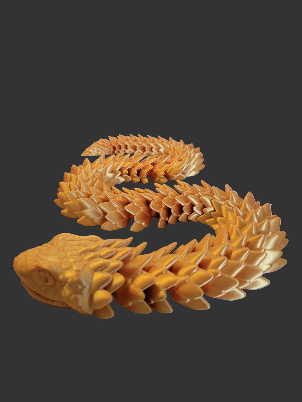 Gold Silk 3D-printed articulated viper with spiky overlapping dragon-like scales in an S shape on a dark gray background.