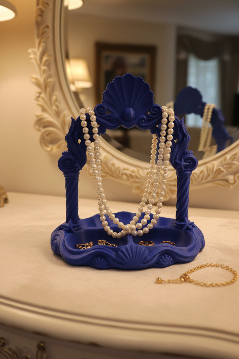 Cobalt Blue 3D-printed oceanic jewelry organizer with a scallop shell arch displaying a pearl necklace over compartments holding rings set on white vanity with mirror.