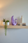 Purple Silk 3D-printed sculpture of swan elegance with detailed wing structure styled with plants and books on a shelf.