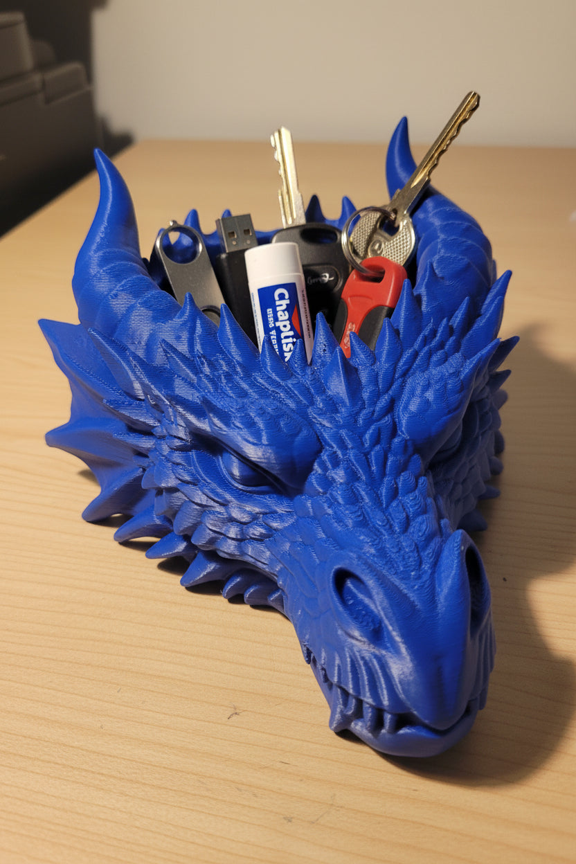 Cobalt Blue 3D-printed catch-all tray with intricate scaling and horns showing teeth while holding multiple items on a wood desk.