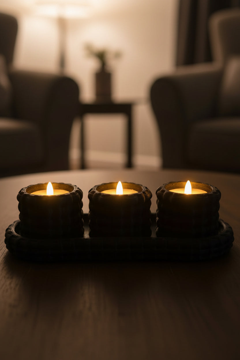 Onyx Black 3D-printed flameless basket woven tea light candle holder set with tray holding 3 glowing warm lights on a coffee table in blurred living room.