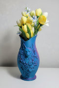 Teal to Pink color-shifting 3D-printed detailed cat vase with raised floral accents holding yellow flowers on a white table.