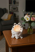 Arctic White 3D-printed ornate Victorian style tea light candle holder with glowing tea light inside decorating a wooden coffee table next to flowers in living room setting.