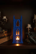 Cobalt Blue 3D-printed tea light holder with towering cathedral design and gothic arched windows glowing on a shelf next to a crow and gothic decor.