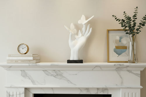 Arctic White 3D-printed hand sculpture with 3 resting butterflies on Onyx Black base displayed on mantel with other decor.