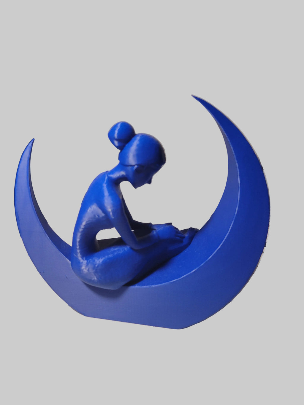 Cobalt Blue 3D-printed sculpture of a woman's profile in a dress resting in a crescent moon on a white background.