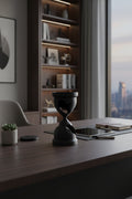 Onyx Black 3D-printed fractured hourglass sculpture with jagged light capturing holes on a modern desk in an office setting.
